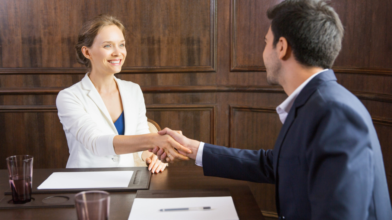 Portrait of young Caucasian businesswoman sitting in conference room and shaking hands with her male partner after finishing meeting