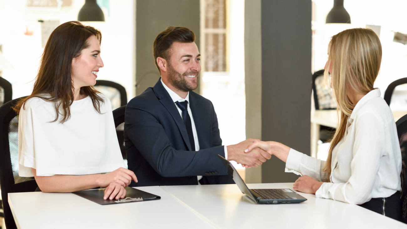 Smiling young couple shaking hands with an insurance agent or investment adviser. Three people meeting in an office reaching an agreement