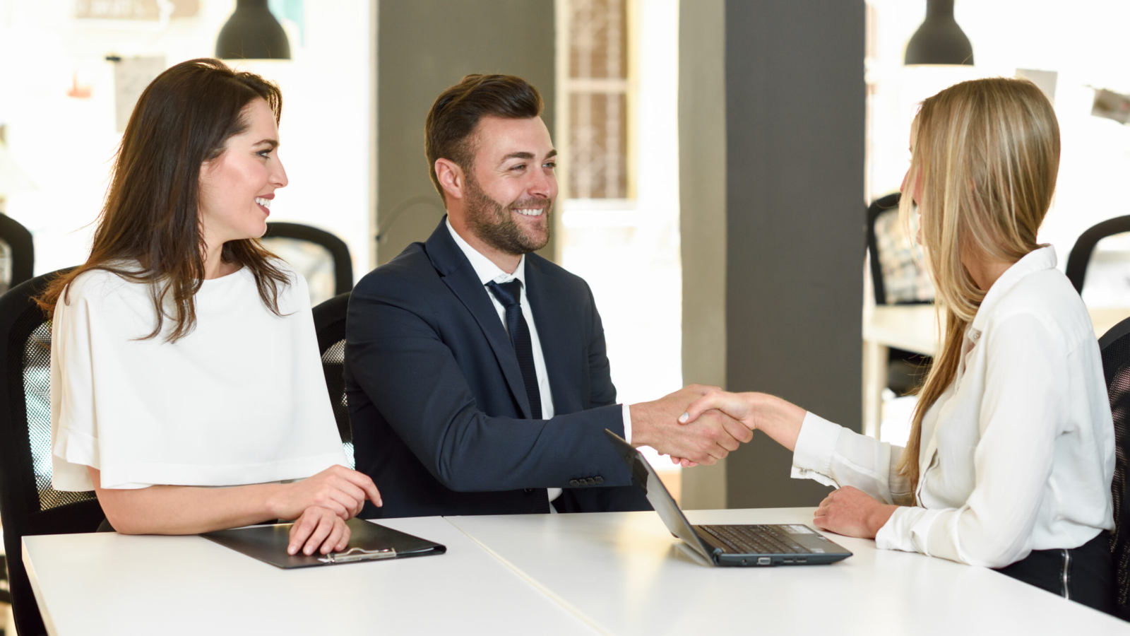 Smiling young couple shaking hands with an insurance agent or investment adviser. Three people meeting in an office reaching an agreement