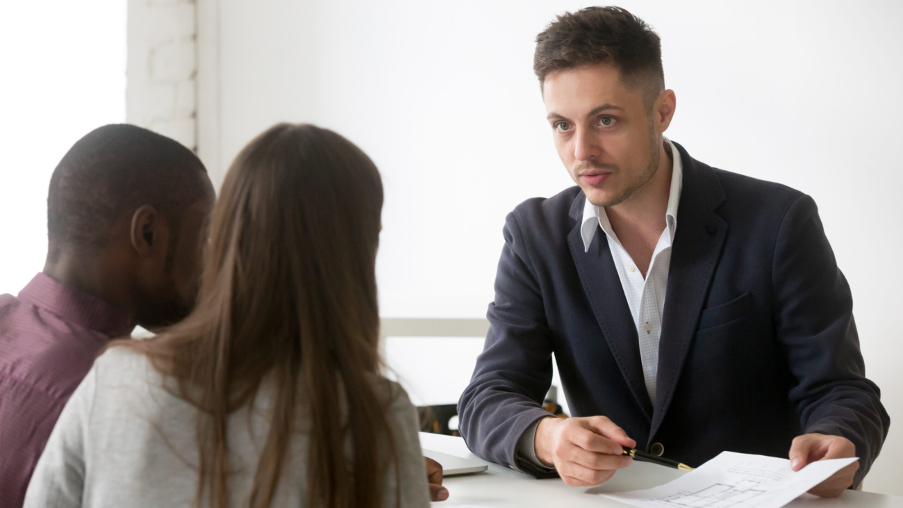 Architect or interior designer showing new house building plan to interracial couple, realtor consulting family customers making real estate offer at meeting, mortgage loan and construction concept