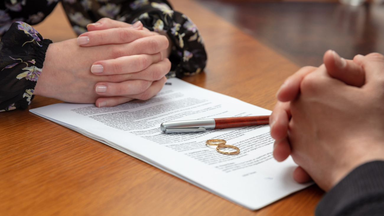 Signing a divorce, marriage dissolution documents and agreement. Wife and husband hands, wedding rings and legal papers for signature on a wooden table, lawyer office