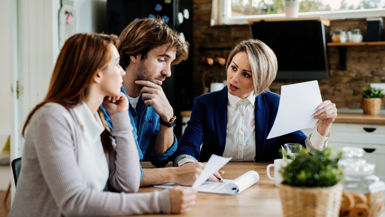 Financial advisor communicating with young couple while going through their financial reports during a meeting at home.